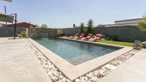 A rectangular swimming pool with a stone border and red lounge chairs. - Superb new contemporary villa with private pool 400 m from the sea  (Agde)