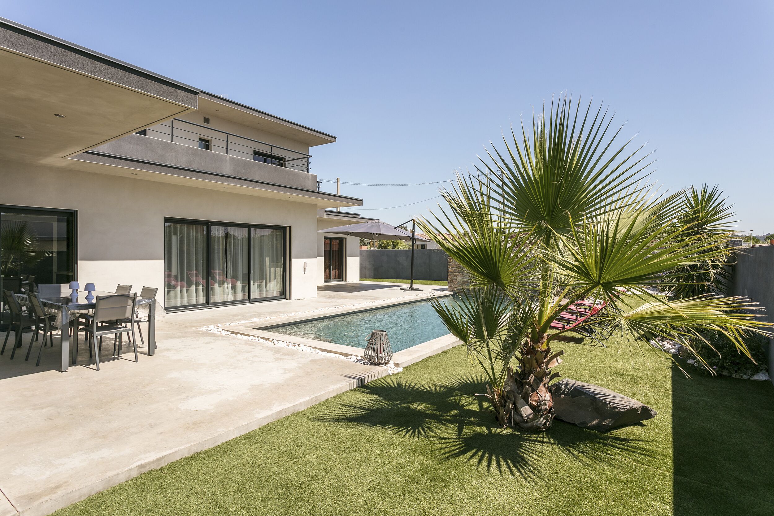 Una casa moderna con piscina, muebles de jardín y un césped bien cuidado.