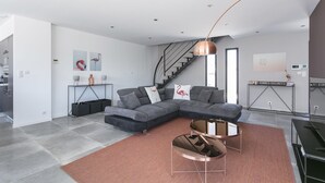 A modern living room with a grey sectional sofa, a round coffee table, and a staircase leading to another level. - Superb new contemporary villa with private pool 400 m from the sea  (Agde)