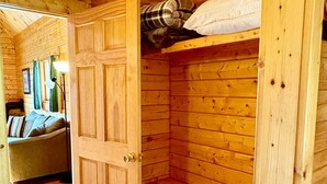 L’intérieur d’un chalet en bois comprend un lit superposé, une porte donnant sur une autre pièce et un couloir avec un canapé.