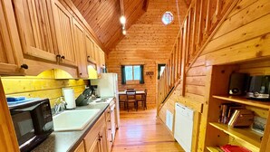 L’intérieur d’une cabane en bois comprend une cuisine, un coin repas et un escalier menant à une mezzanine.