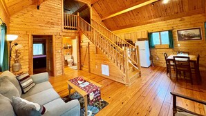 L’intérieur de cette vaste cabane en rondins est doté d’un escalier central, d’un coin repas et d’un salon aménagé avec un canapé et une table basse.
