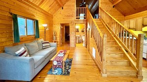 L’intérieur d’un chalet chaleureux, avec un escalier en bois, un canapé et un coin repas.