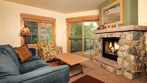 A cozy living room with a stone fireplace, a sofa, a patterned armchair, and a table. - Charming Condo in the Heart of River Run Village (Dillon)