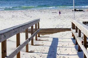 Une promenade en bois menant à une plage, avec une personne visible au loin.