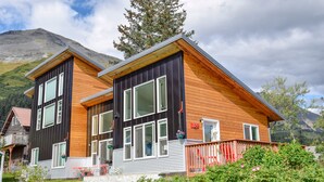 A modern two-story house with a wooden facade and large windows, set against a mountainous backdrop. - Modern Accommodations with Luxurious View (Seward)