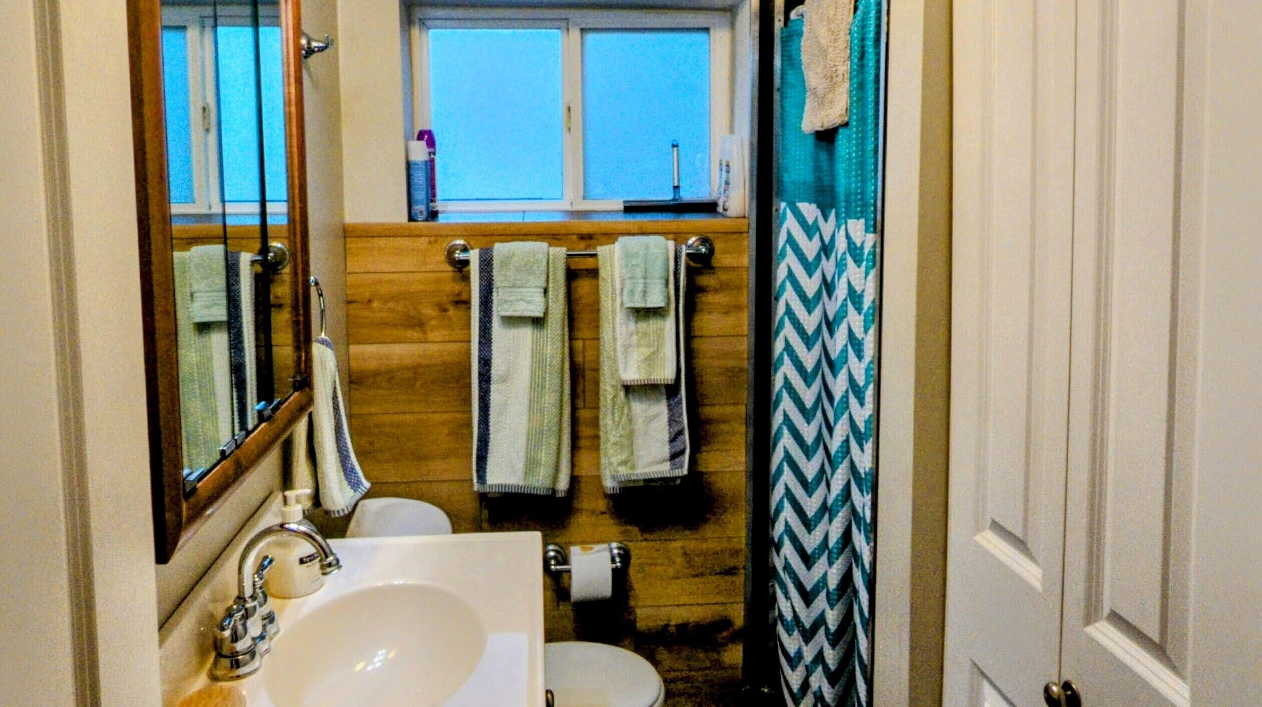 Un baño con tocador de madera, un lavamanos, un inodoro y una ventana sobre el inodoro.