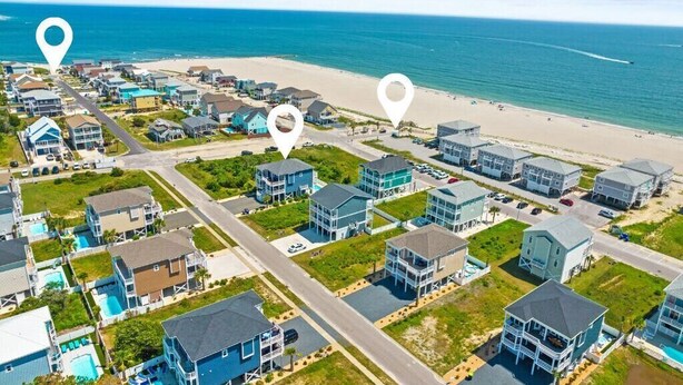 Vue aérienne d’une zone résidentielle côtière, avec des maisons, une plage et une route.