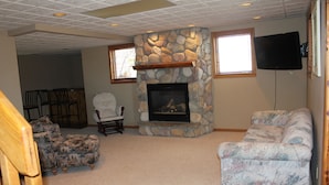 A living room with a stone fireplace, a television mounted on the wall, and a couch.