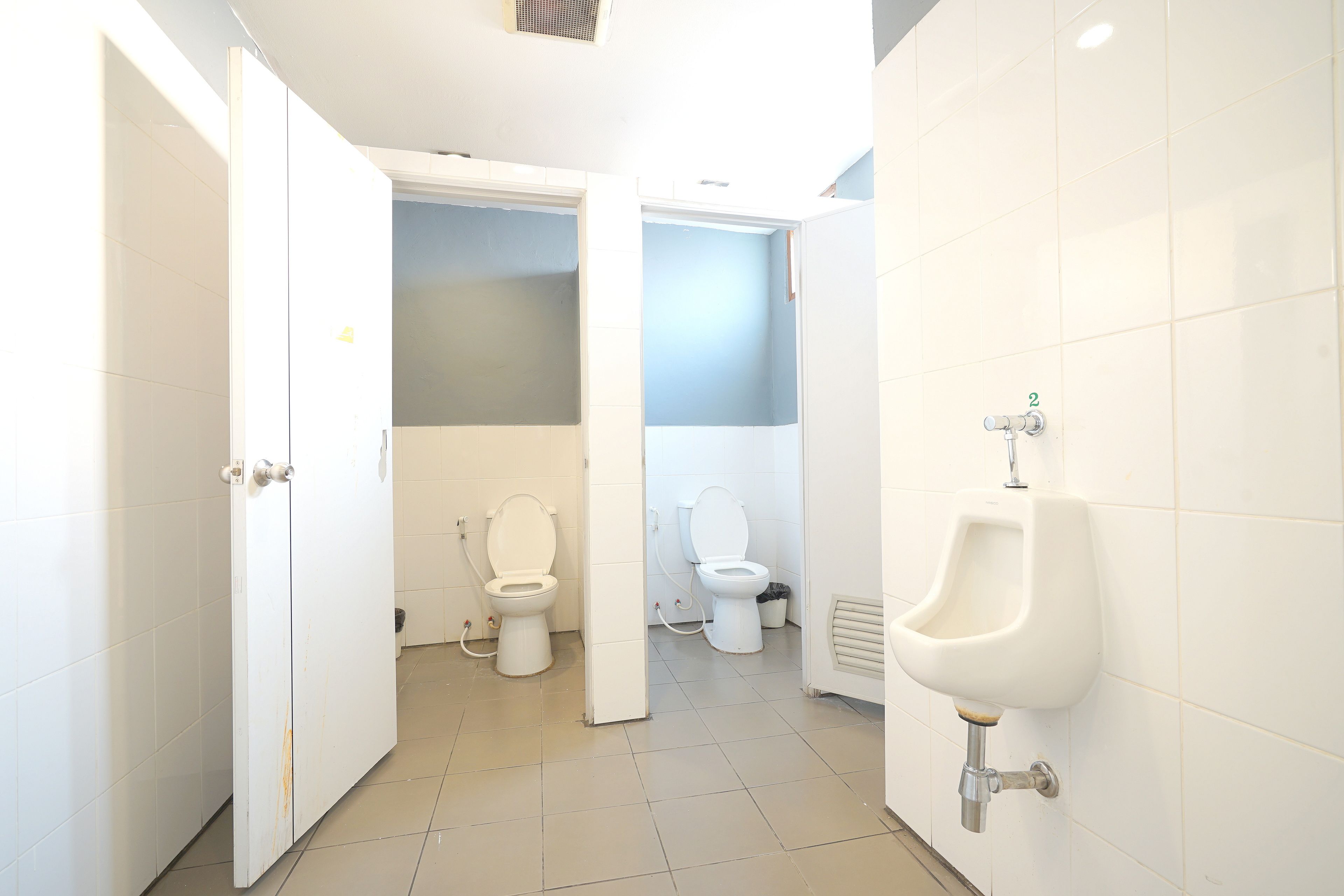 A bathroom with two toilets, a urinal, and white tiled walls.