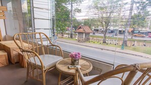 Ein Zimmer mit Korbmöbeln, einem kleinen runden Tisch mit einer Vase und Blick auf die Straße.