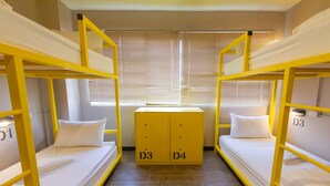 Ein Schlafsaalzimmer mit Etagenbetten, einem zentralen Schreibtisch und einem Fenster mit Jalousien.