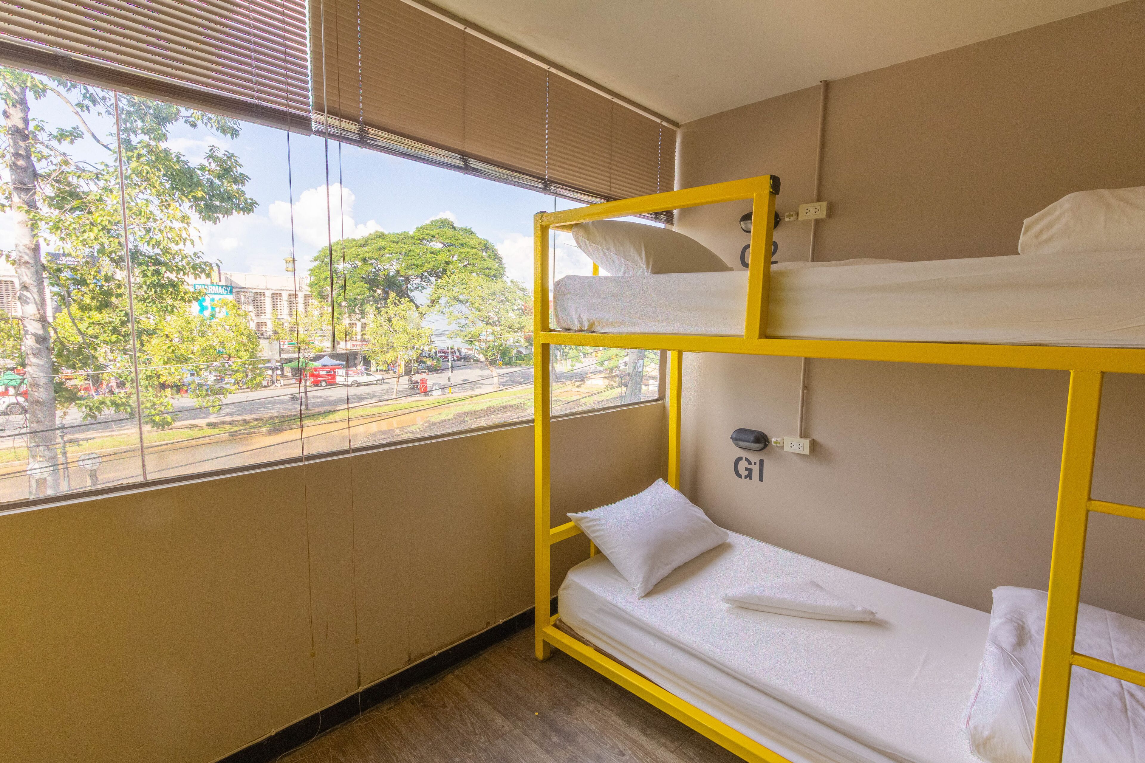 Quarto com beliche e vista pela janela para a rua e árvores.