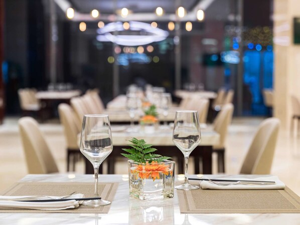 Une salle à manger de restaurant avec des tables préparées pour deux personnes, chacune agrémentée d’un verre à vin et d’un petit vase avec des fleurs.