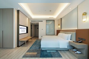 A modern hotel room with a bed, bedside table, and a television displaying 'NOVOTEL.' - Novotel Wuxi (Wuxi)