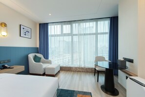 A hotel room with a bed, a desk, a chair, a table, and a large window with curtains. - Novotel Wuxi (Wuxi)