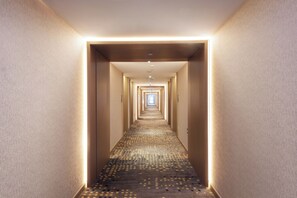 A hotel hallway with a patterned carpet, light-colored walls, and a series of doors leading to rooms. - Novotel Wuxi (Wuxi)