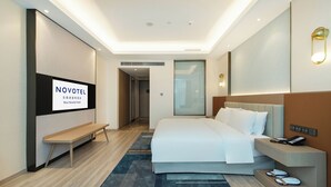 Moderni hotellihuone, jossa on sänky, yöpöytä ja televisio, jossa näkyy teksti »NOVOTEL».