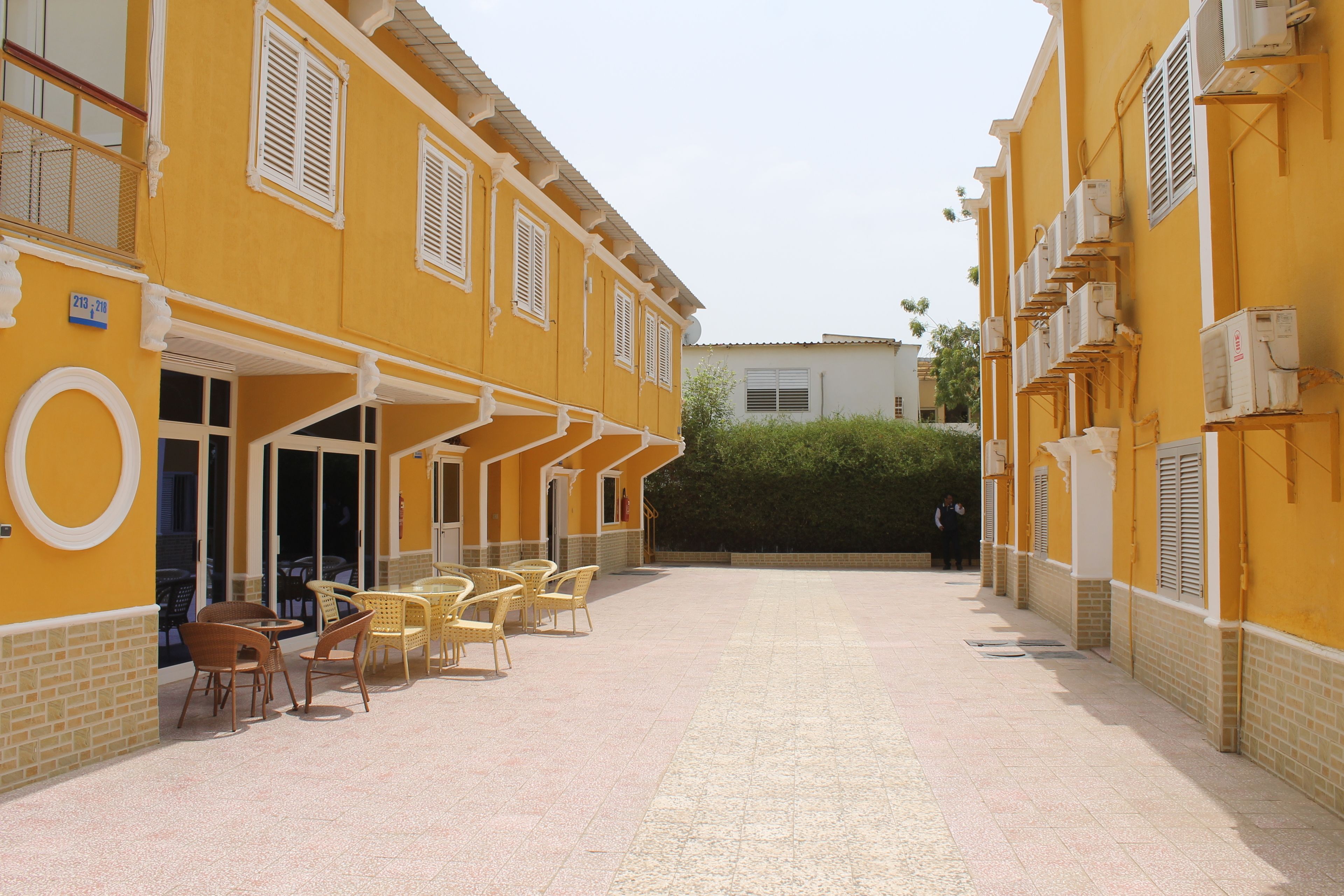 Une cour intérieure bordée de bâtiments jaunes, avec des espaces de repos en plein air et des unités de climatisation.