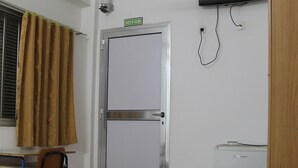 Une chambre d’hôtel comprenant un lit, un bureau, une chaise, un téléviseur fixé au mur, une porte et un petit réfrigérateur.