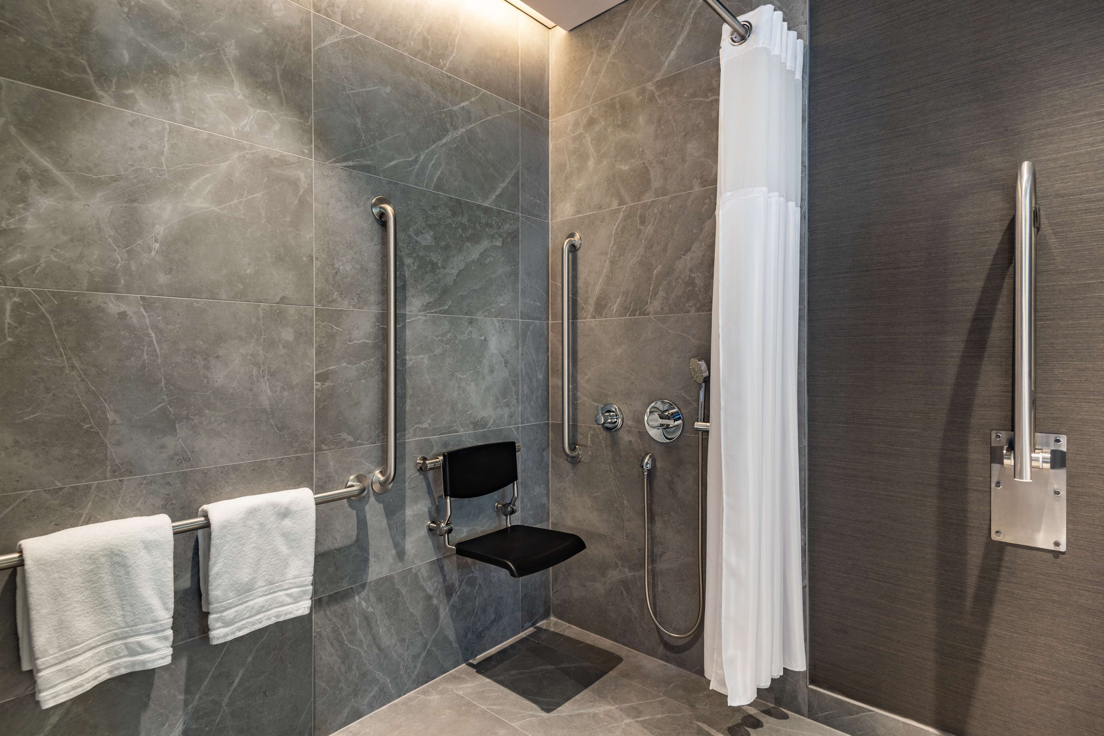 Une salle de bain moderne équipée d’une douche, de barres d’appui, d’un banc et d’un porte-serviettes.