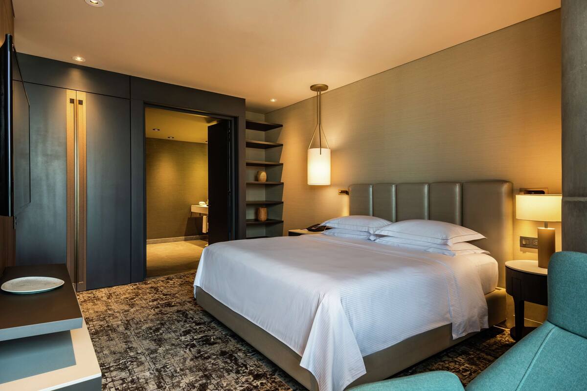 Una habitación de hotel moderna con una cama grande, un escritorio, una silla y estanterías integradas.