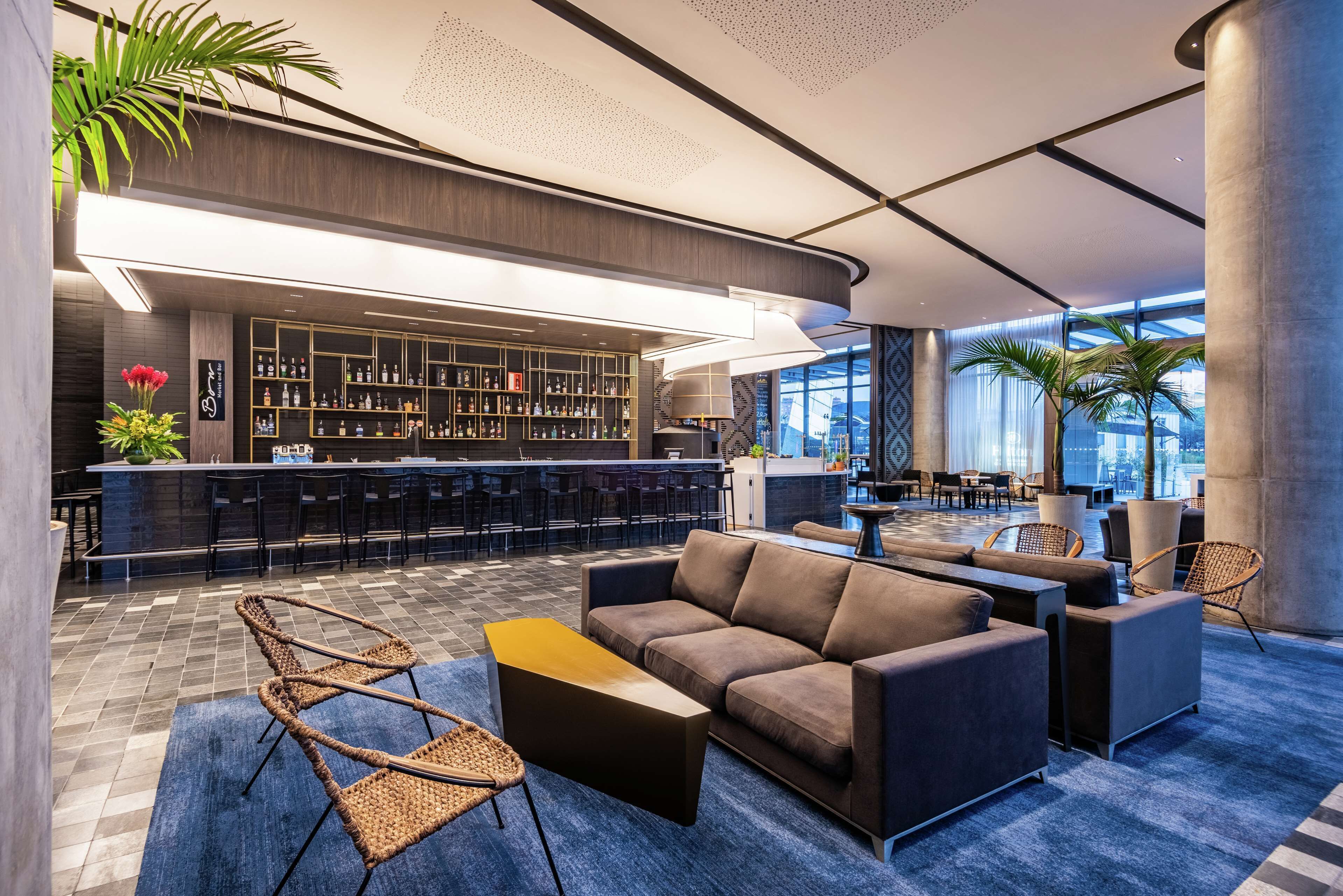 A modern bar area with a bar counter, seating, and a large window providing a view of the city.