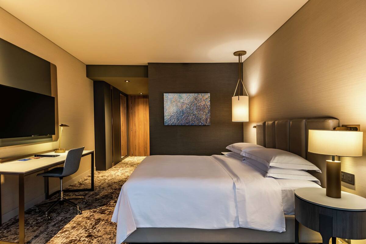 Habitación de hotel con cama, escritorio, silla, televisor y una obra de arte en la pared.