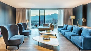 A modern living room with a city view, featuring a sofa, armchairs, a coffee table, and a lamp.