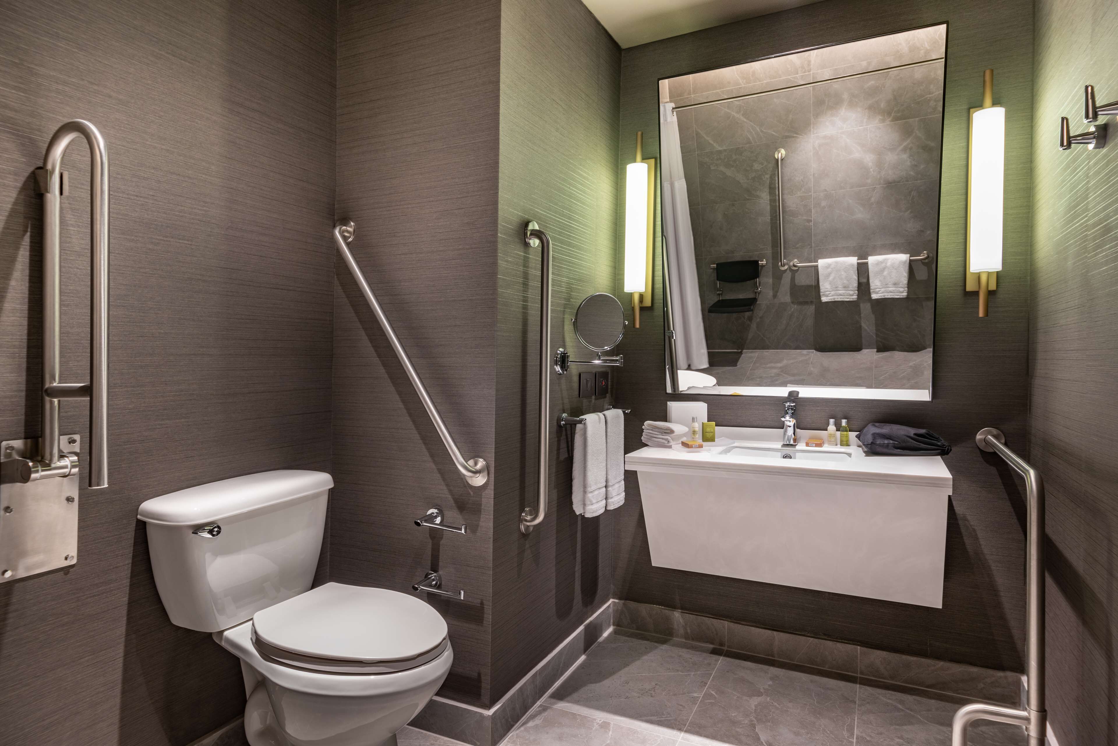 A modern bathroom with a toilet, bidet, and sink, equipped with grab bars and a mirror.