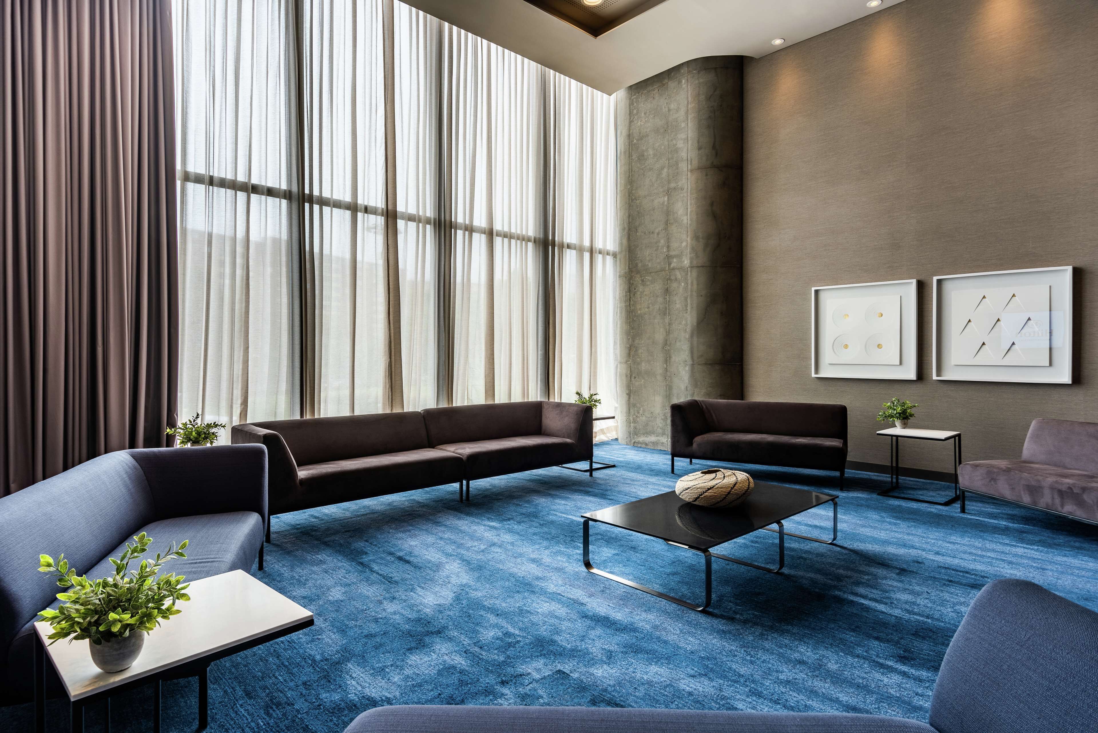 Un salon moderne avec une moquette bleue, des canapés foncés, une table basse et deux œuvres d’art encadrées accrochées au mur.