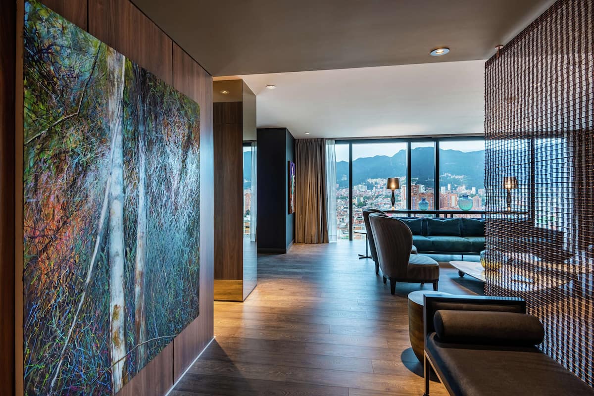 Una habitación de hotel moderna con un cuadro abstracto grande, vistas a la ciudad y una zona de estar acogedora.