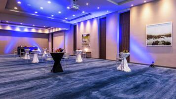 Una sala de conferencias con alfombra azul, mesas blancas cubiertas con manteles blancos y una pantalla de proyector.