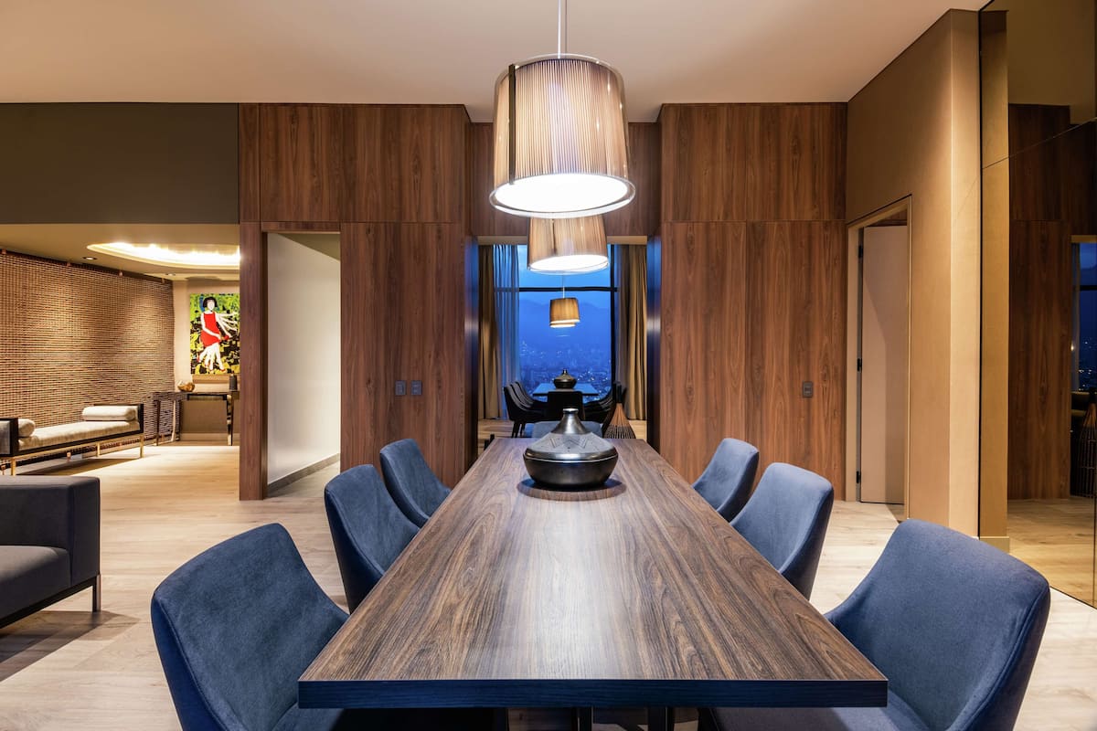 Un comedor moderno con una larga mesa de madera, sillas tapizadas en azul y una lámpara colgante.