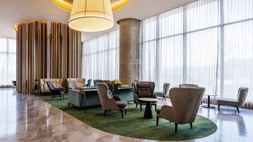 A spacious lobby with a curved green carpet, modern seating, a large pillar, and large windows.