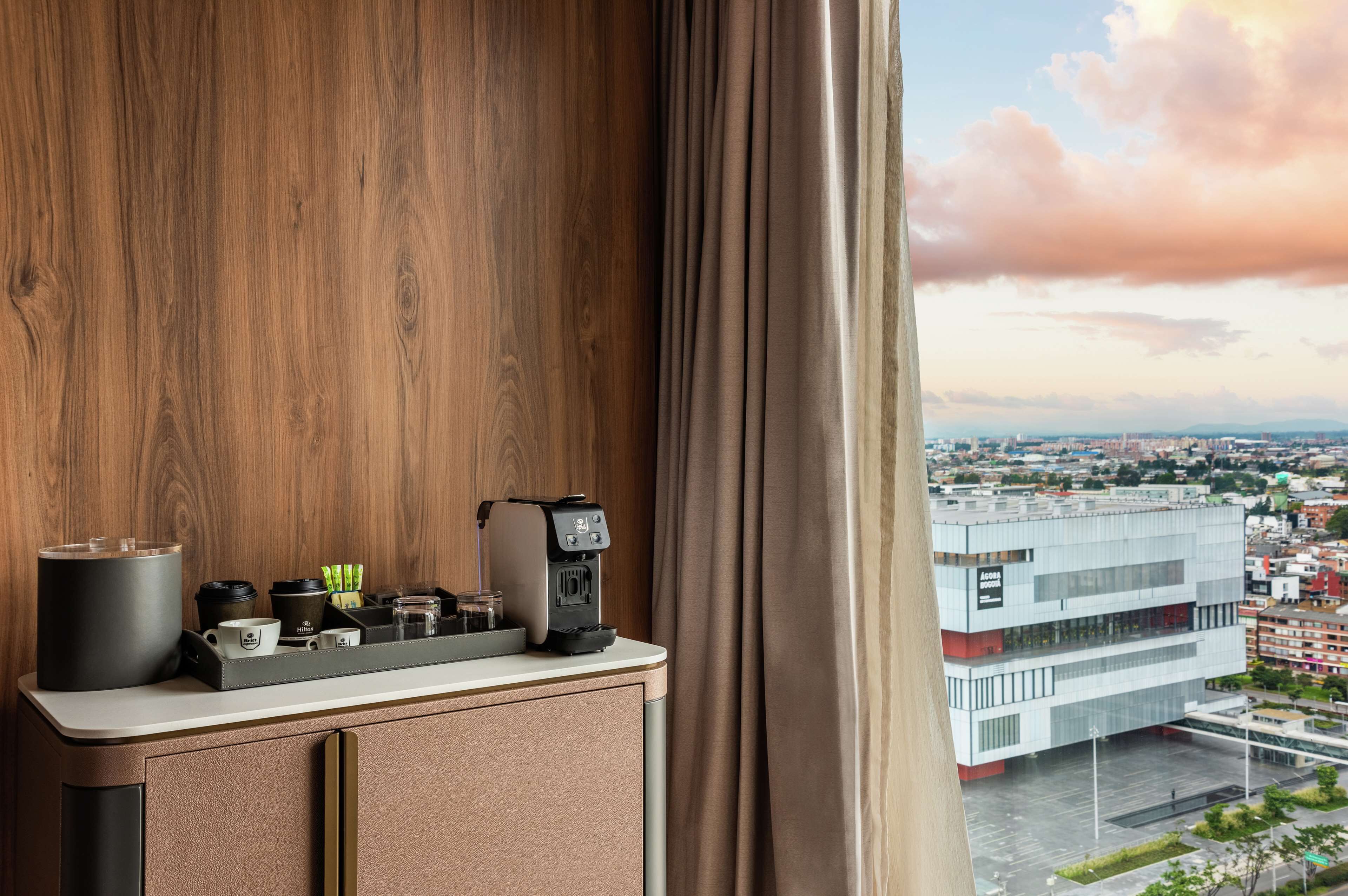 A modern hotel room with a coffee station, a view of the cityscape, and a large window with curtains.
