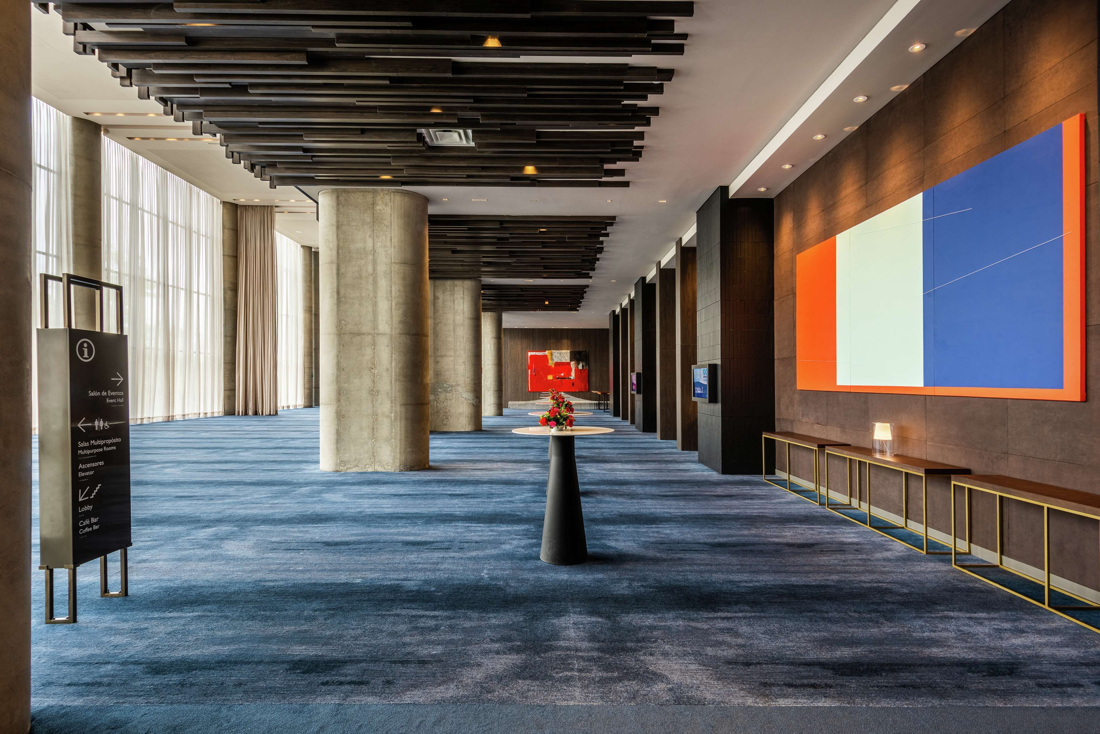 A spacious corridor with a blue carpet, large columns, and a modern ceiling design.