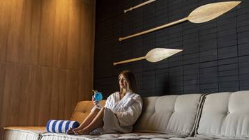 A person sitting on a sofa in a room with a wooden panel wall and a black grid wall with wooden paddles.