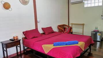 A bedroom with a bed, a chair, a small table, an air conditioner, and a window.