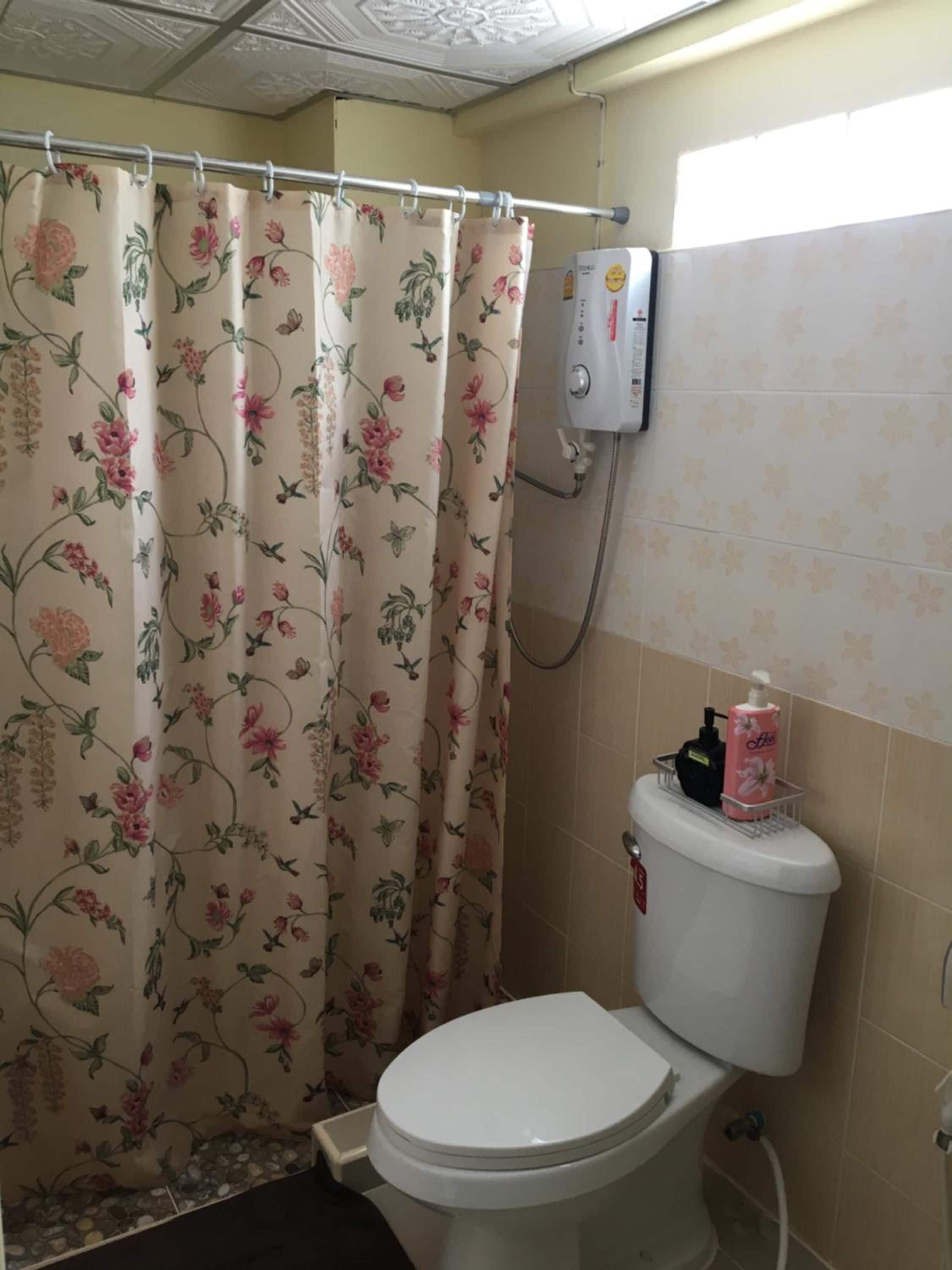 Een badkamer met toilet, een douchegordijn met bloemenmotieven en een wandwaterverwarmer.