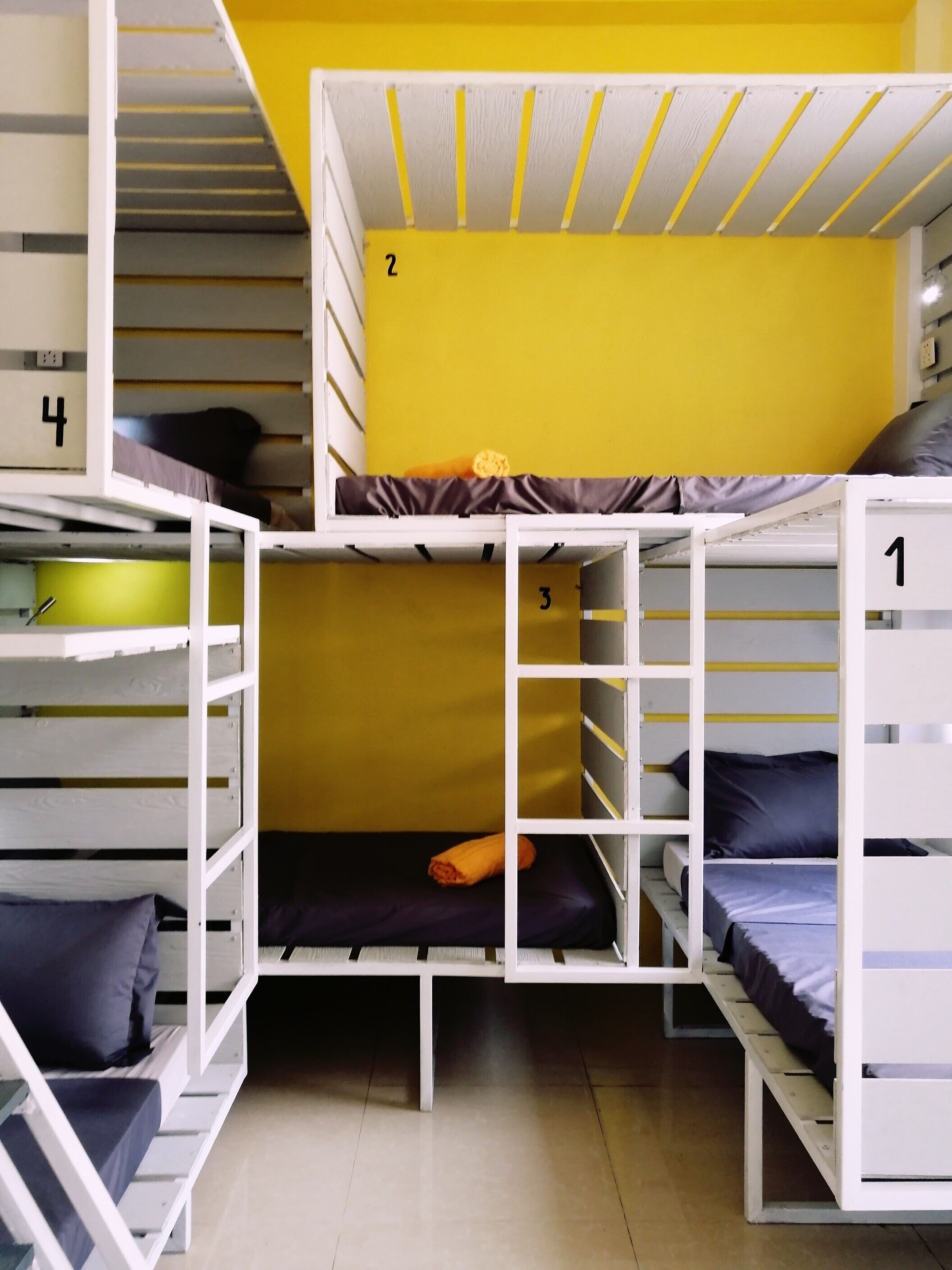 A multi-level bunk bed room with numbered beds, a yellow wall, and a tiled floor.