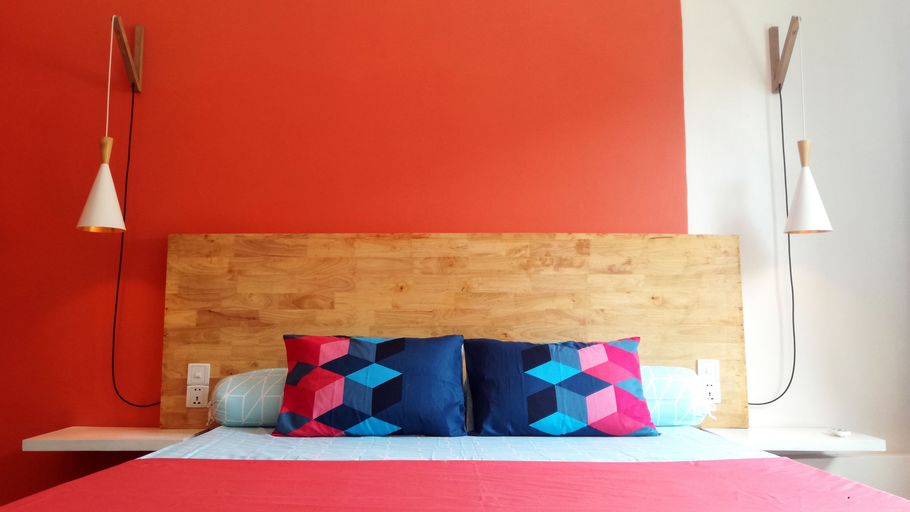 Una cama con cabecera de madera, dos almohadas con diseños geométricos y dos lámparas colgantes a cada lado.