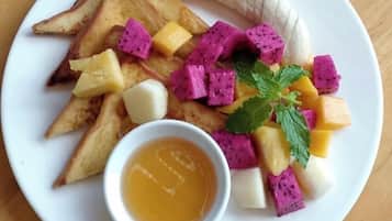 Een bord met toast, banaan, pitahaya, mango en een klein schaaltje siroop.