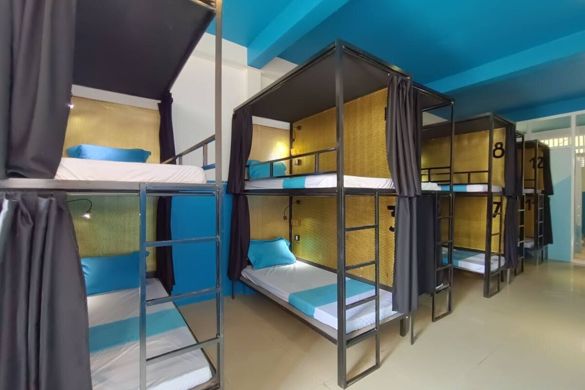 A dormitory-style room with bunk beds, curtains, and a blue ceiling.