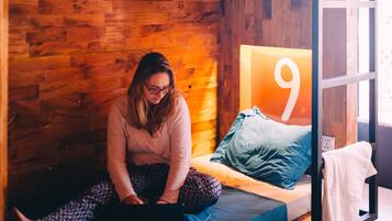 Habitación con literas, una pared de madera, ropa de cama azul y gris, y un cartel con el número 9 en la pared.