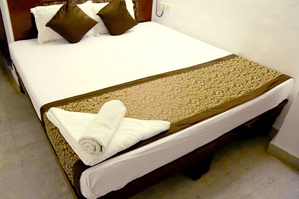 Ein ordentlich bezogenes Bett mit weißer Decke, braunen Kissen und einer braunen Zierdecke.