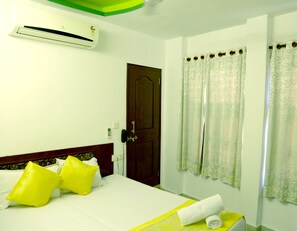 A hotel room with a bed, a telephone, an air conditioning unit, and curtains.
