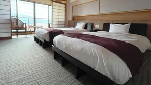 Habitación de hotel con dos camas, cabecera de madera, un ventanal y vista al mar.