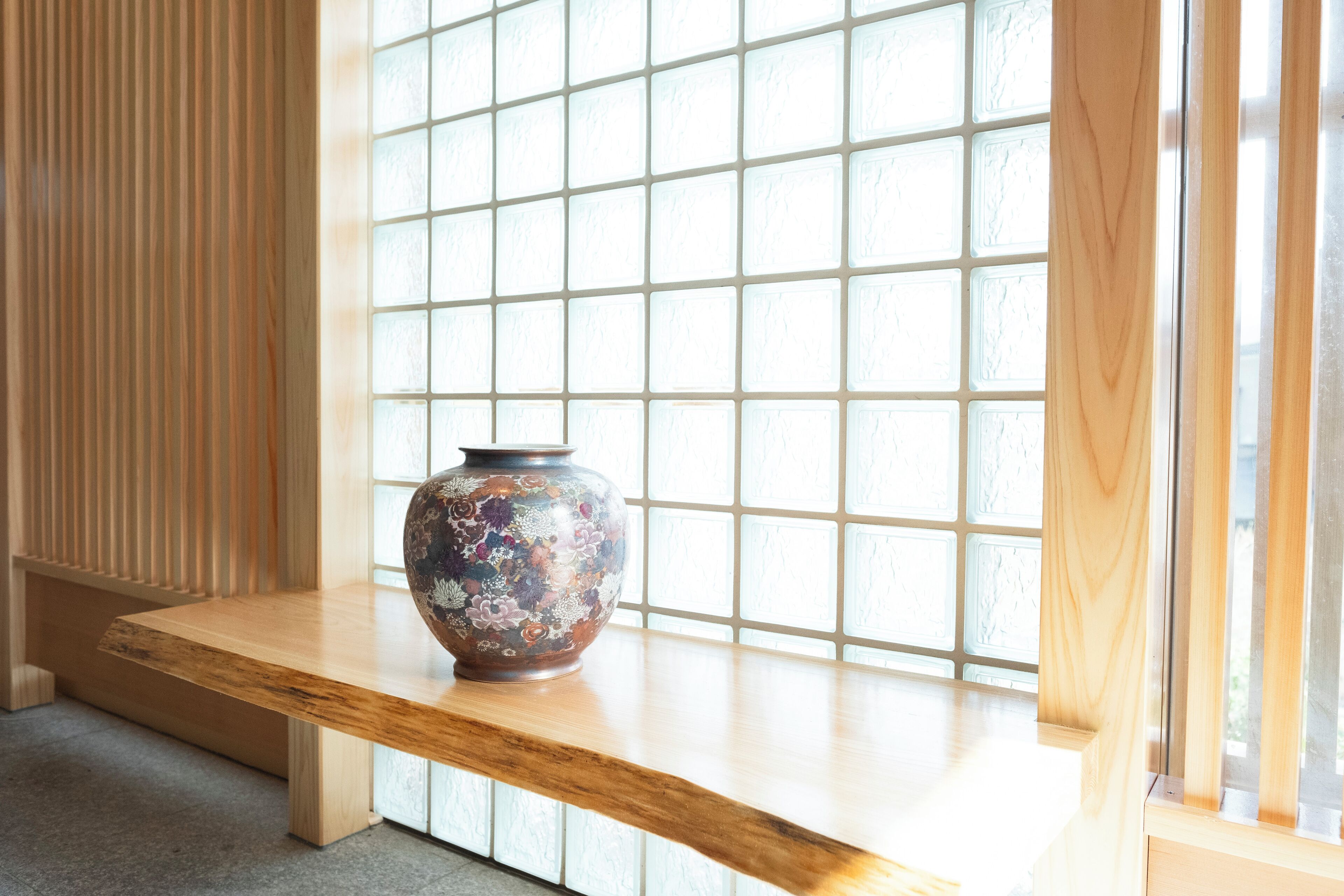A wooden shelf with a decorative vase against a window with a grid pattern.