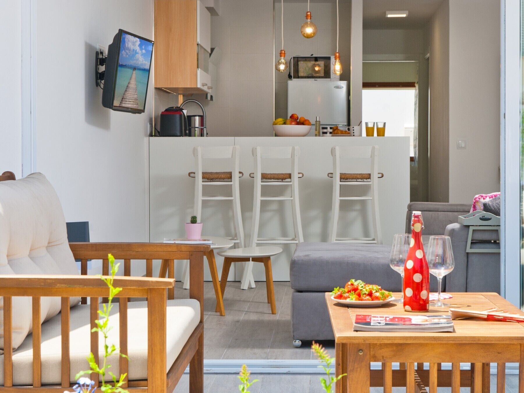 Een moderne woonkamer met een bank, een houten tafel en een eethoek met stoelen. Achtergrond is een keuken met een koelkast en een magnetron.